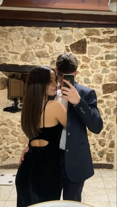 a man and woman taking a selfie in front of a stone wall with a camera