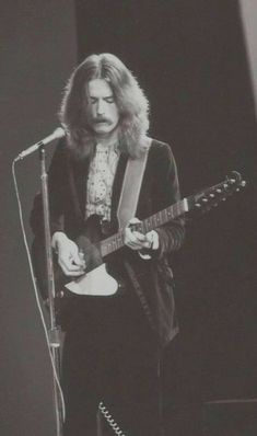 a man with long hair playing a guitar in front of a microphone while standing on stage