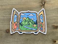 a sticker with an image of a bus window and mountains in the background on a wooden surface