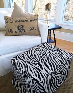 a zebra print ottoman sitting next to a white couch with a pillow on top of it