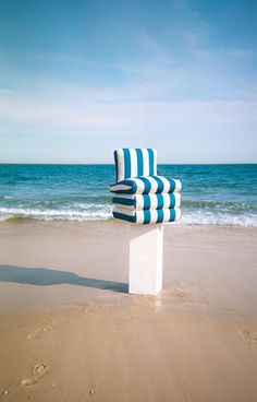 a blue and white chair sitting on top of a sandy beach next to the ocean