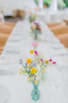 a long table with flowers in vases and empty wine glasses on the table top