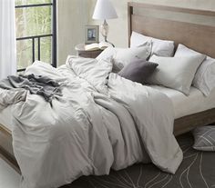 an unmade bed with white sheets and pillows in front of a large windowsill