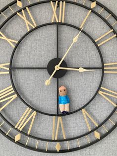 a clock with a small wooden figure on it's face in front of a gray background