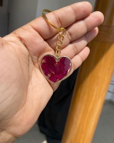 a person holding a heart shaped keychain with a red stone in the middle