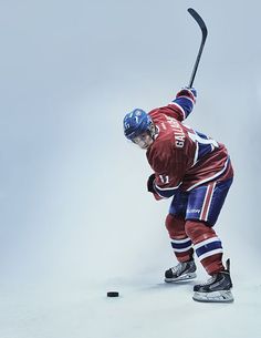 an ice hockey player in red jersey and blue pants is holding a stick with both hands