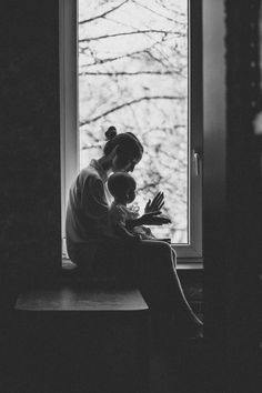 two women sitting on a window sill looking out the window