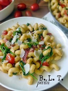 pasta with tomatoes and spinach in a white bowl on a wooden table next to other dishes