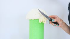 a woman is holding a knife and cutting into a green vase with white frosting