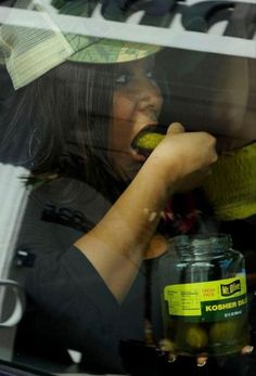 a woman in a hat eating something out of a jar while sitting in the back seat of a car