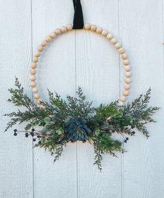 a wreath made out of wood beads and greenery hangs on a white wooden wall