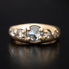 a gold ring with three stones on top and two diamonds in the middle, sitting on a black surface