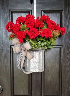 a metal bucket with red flowers hanging from it's front door and tied to the handle