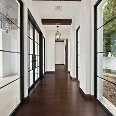 an empty hallway with wood flooring and large windows on either side of the room