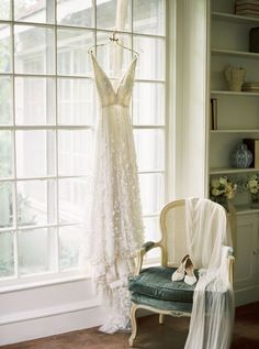 a wedding dress hanging on a window sill in front of a chair with a veil draped over it