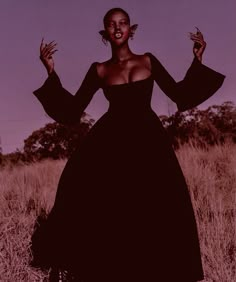 a woman in a black dress is standing in a field with her hands out to the side