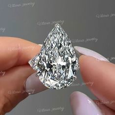 a close up of a person's hand holding a fancy ring with a pear shaped diamond