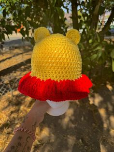 a hand holding a knitted hat in the shape of winnie the pooh with ears