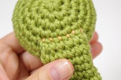 a hand holding a green crocheted object in it's palm