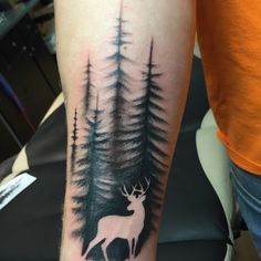 a man's arm with a deer and pine trees tattoo on the left forearm