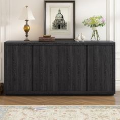 a black cabinet sitting on top of a wooden floor next to a lamp and pictures