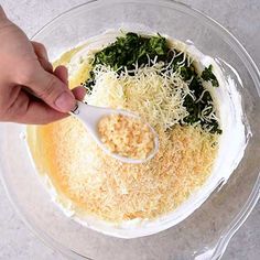 someone is adding cheese and spinach to a dish in a glass bowl with a spoon