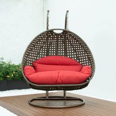 a hanging egg chair with red cushions on a wooden deck next to a potted plant