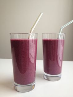 two glasses filled with purple smoothie on top of a white table next to each other