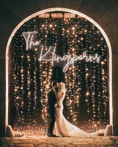 a bride and groom standing in front of an archway covered with fairy lights