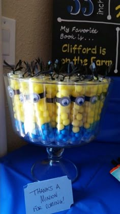 a glass bowl filled with yellow and blue candies in front of a sign that says, my favorite book is cliffford is on the farm