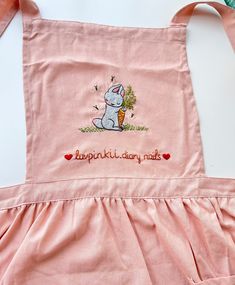 a pink apron with an embroidered bunny holding a carrot in it's right hand