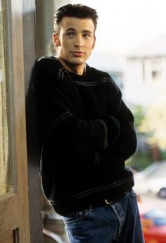 a young man leaning against a door with his arms crossed and looking at the camera