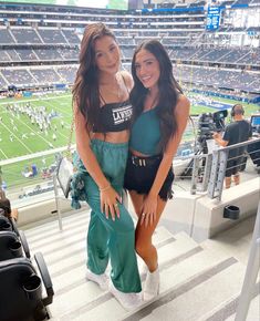 two beautiful women standing next to each other in front of a stadium filled with people