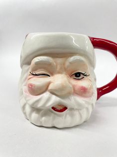 a ceramic mug with a santa claus face on it's side and red handle