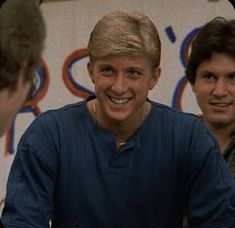 three young men sitting at a table with food in front of them and one smiling