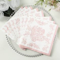 four pink and white napkins on a chain next to flowers, pearls and beads