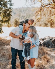 a man and woman holding a baby while standing next to each other in a field