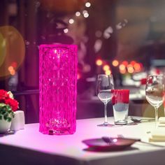 a pink vase sitting on top of a table next to two wine glasses and plates