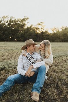 a man and woman sitting on the ground in a field, one holding a camera