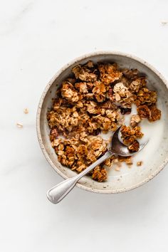 a bowl filled with granola on top of a white counter next to a spoon