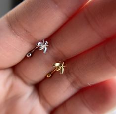 a person's hand holding two tiny gold and silver ear studs on top of each other