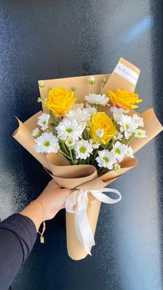 a person holding a bouquet of flowers on top of a blue surface with white and yellow daisies