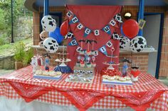 a red and white table topped with desserts and balloons in front of a building