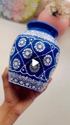 a hand holding a blue vase with white designs on it