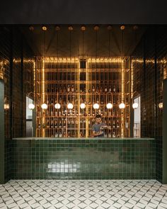 a man sitting at a bar in front of a green tiled wall with lights on it