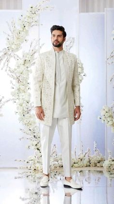 a man in a white outfit standing next to a floral wall with flowers on it