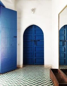 an empty room with blue doors and chevron tile flooring in front of two mirrors