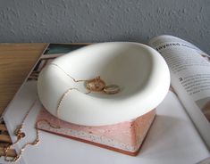 a white ring dish sitting on top of a table next to an open book with a chain