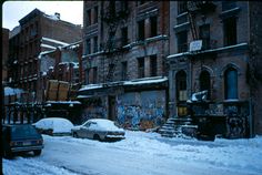 cars are parked on the street in front of buildings with graffiti all over them and snow covered ground