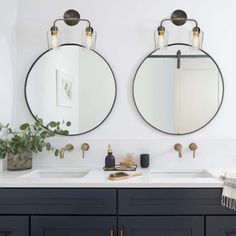 two round mirrors are above the double sinks in this bathroom with dark blue cabinets and brass fixtures